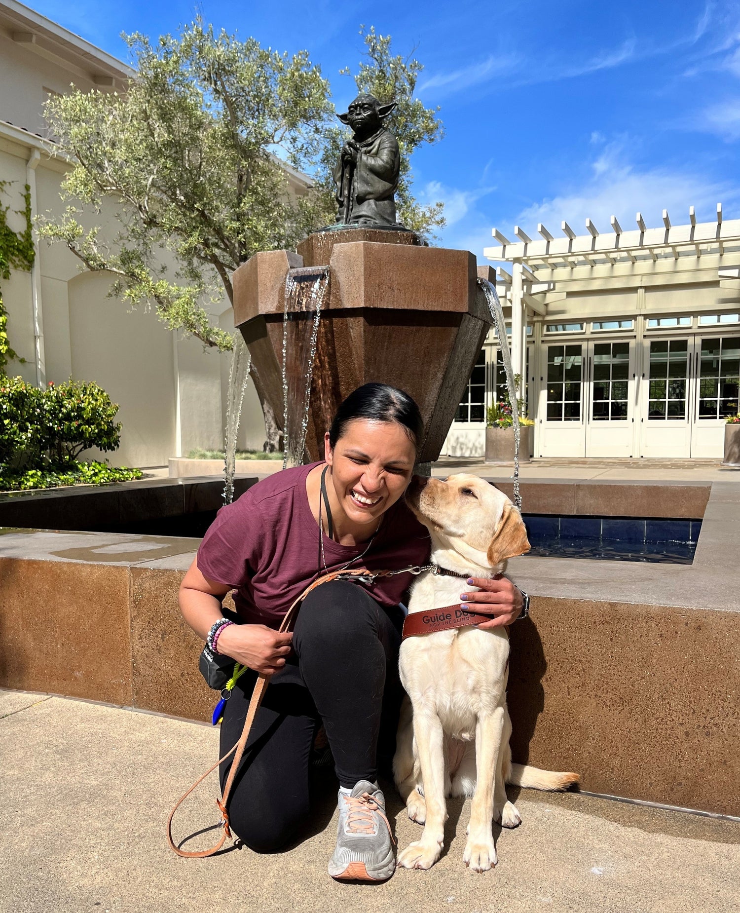 Christella with her guide dog, Frolic, kissing her in front of a Yoda statue.